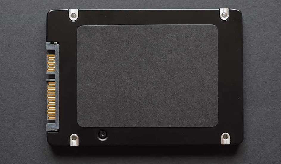 Vue rapprochée d'un disque SSD noir avec connecteur doré, fixations argentées et étiquette centrale.