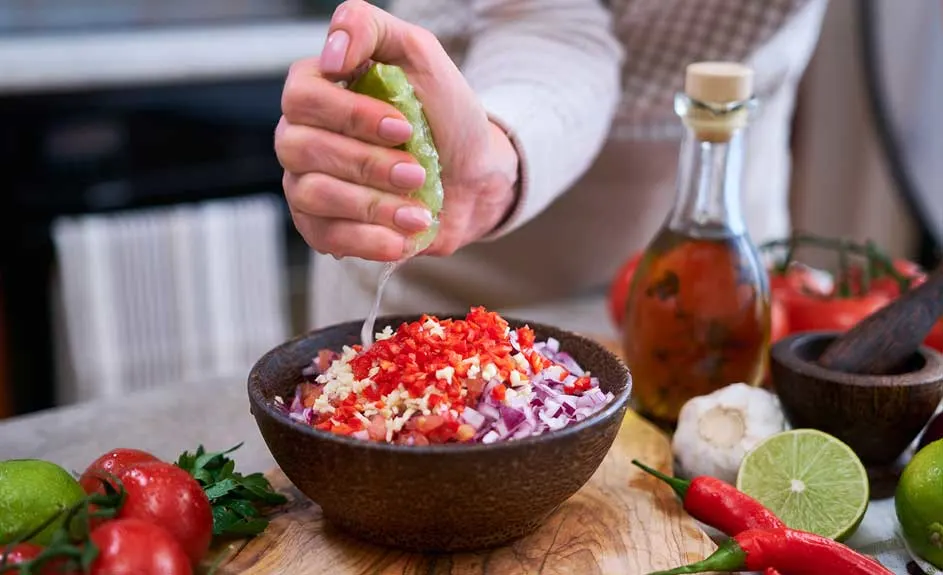 Bol rempli de dés rouges, blancs et violets, avec du jus de citron vert pressé dessus. Huile, légumes et mortier en bois à l'arrière.