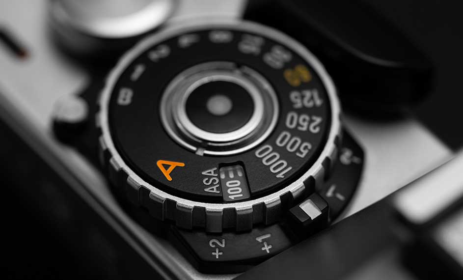 Réglage de l'appareil photo argentique : molette noire avec chiffres blancs, ASA 100 en évidence, lettre "A" orange.