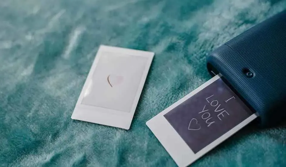 Deux photos instantanées sur un tissu bleu doux. L'une sort d'une imprimante bleue, affichant "I Love You".