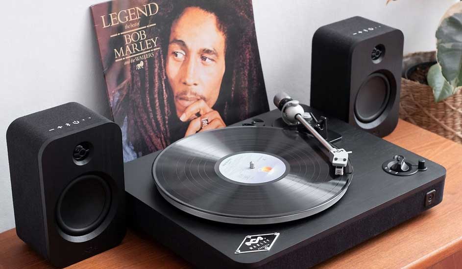 Platine vinyle noire avec haut-parleurs, album "Legend" de Bob Marley en arrière-plan sur une table en bois.