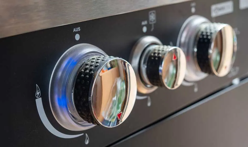 Gros plan sur trois boutons de commande chromés sur une plaque de cuisson noire, avec des indicateurs de réglage.