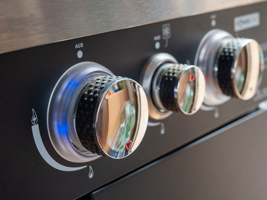 Gros plan sur trois boutons de commande chromés sur une plaque de cuisson noire, avec des indicateurs de réglage.