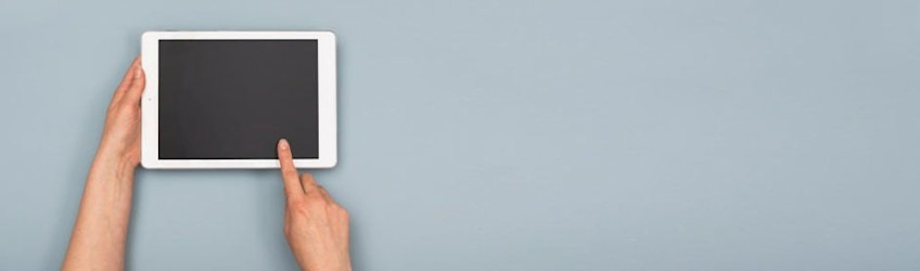 A white tablet with a black screen is held and touched against a light blue background.