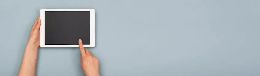 A white tablet with a black screen is held and touched against a light blue background.