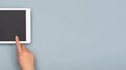 A white tablet with a black screen is held and touched against a light blue background.