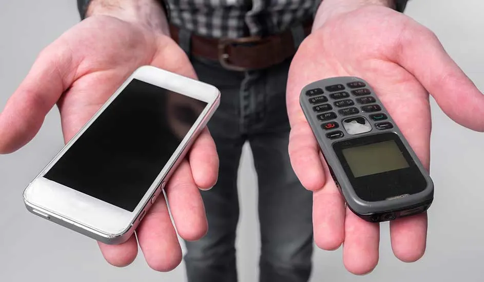 Deux mains tenant un smartphone blanc et un ancien téléphone gris à boutons sur un fond gris clair.