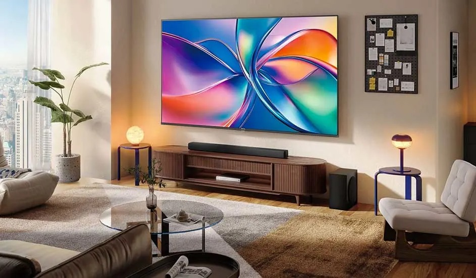 Spacious living room with a huge TV showing vivid abstract colors, modern furniture and a wide view over the city skyline.