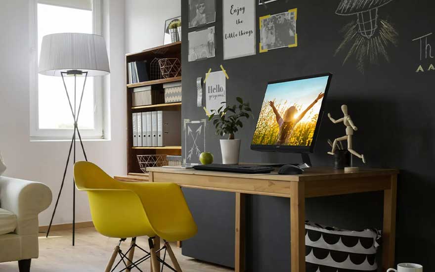 Bureau avec ordinateur sur mur noir, chaise jaune, bibliothèque et lampe.