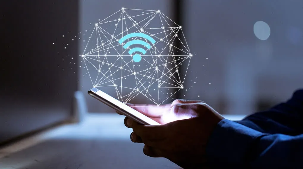 Une personne tient un smartphone avec un symbole Wi-Fi bleu dans un réseau de lignes blanches. L'arrière-plan est sombre.