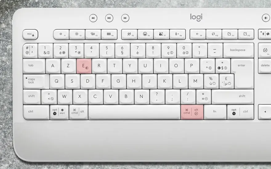 Clavier blanc Logitech avec touches E et CMD en rose, sur fond gris. Les touches affichent des lettres et symboles.