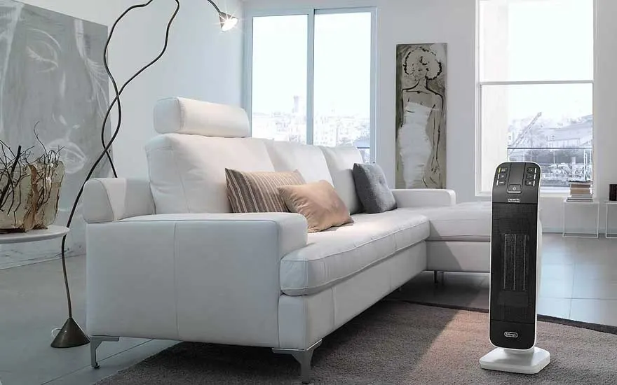 Witte sofa met kussens in een lichte woonkamer, staande lamp en een zwarte elektrische kachel.