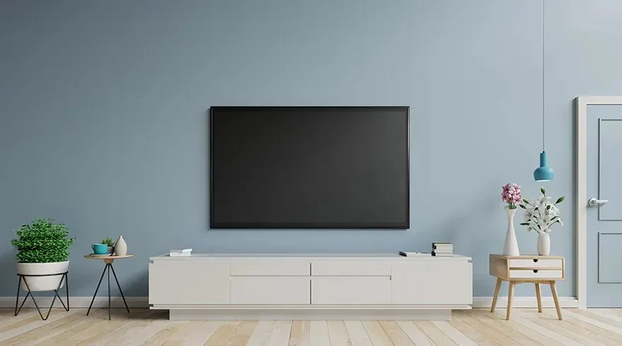 Salon bleu clair avec une télévision noire, un meuble blanc, une table de chevet en bois et un sol en bois clair.