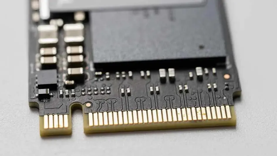 Een close-up van een zwarte geheugenkaart met gouden connectoren en kleine elektronische componenten, liggend op een lichtgrijze ondergrond.