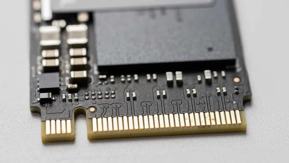 Un gros plan d’une carte mémoire noire avec des connecteurs dorés et de petits composants électroniques, posée sur un fond gris clair.