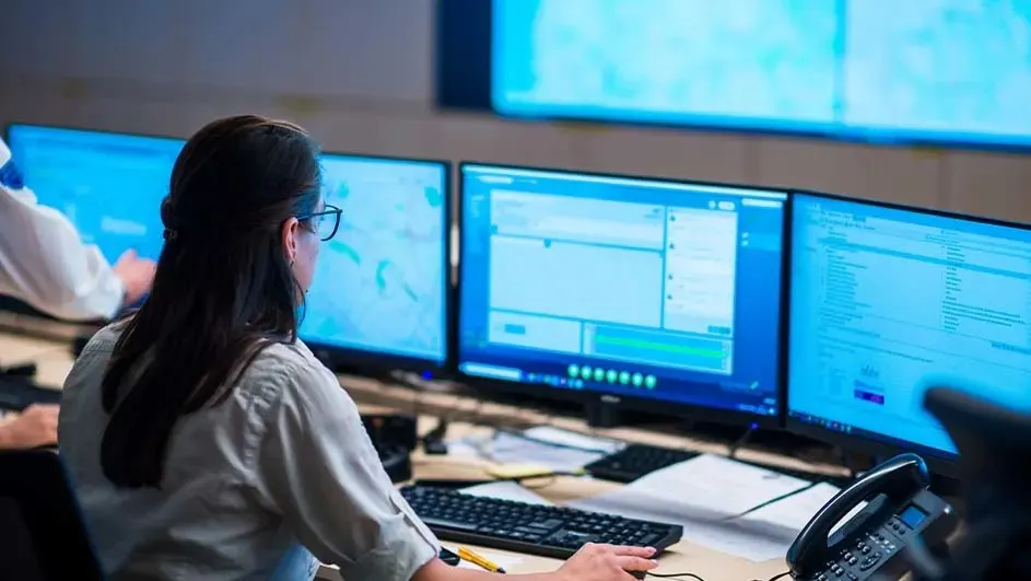 Een bureau met drie blauwe computerschermen, een toetsenbord, een telefoon en een muis.