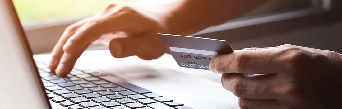 Hands type on a laptop keyboard while holding a gray credit card, indoors.