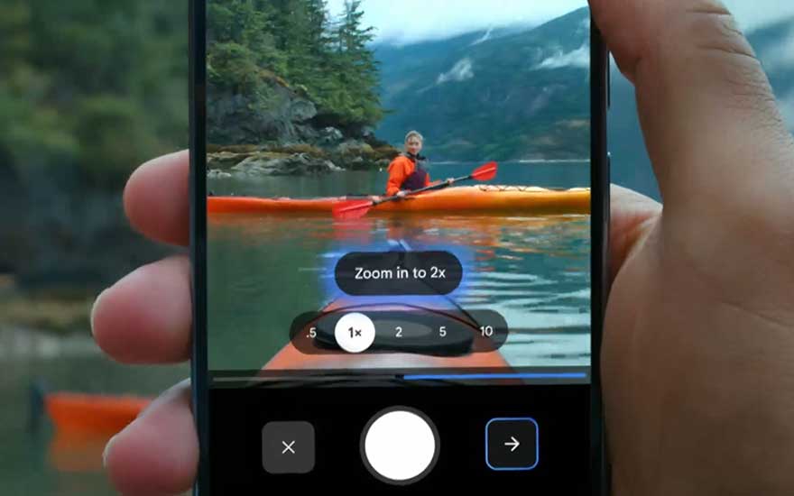 Smartphone displays camera function with zoom options whilst someone paddles orange kayak on mountain lake amongst green forests and hills.