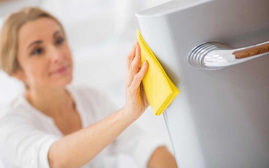 Une main tenant un chiffon jaune nettoie une porte grise avec une poignée argentée dans une pièce lumineuse.