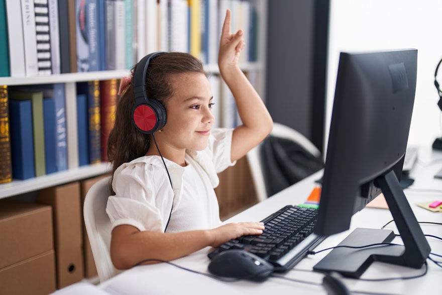 Une table blanche avec un ordinateur, un clavier et une souris noirs. Une étagère pleine de livres colorés est visible en arrière-plan.