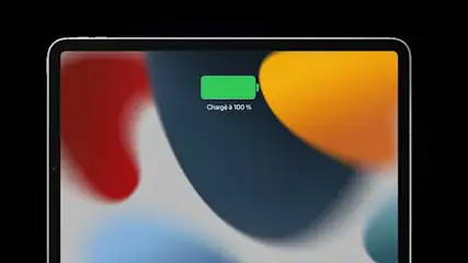 Tablette avec écran affichant une batterie verte chargée à 100%, sur fond coloré abstrait.