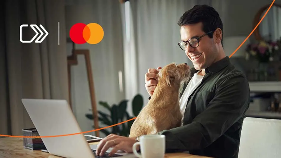 Een laptop staat op een bureau, met een mok, een hond en het Mastercard-logo op de achtergrond.