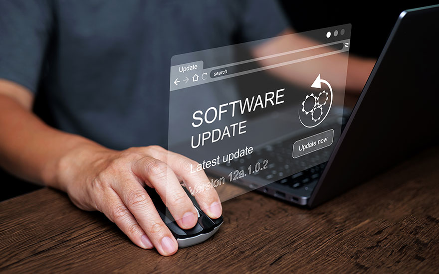 Mise à jour du logiciel sur un ordinateur portable. Main sur une souris noire. Fenêtre de mise à jour avec texte blanc. Fond de table en bois.