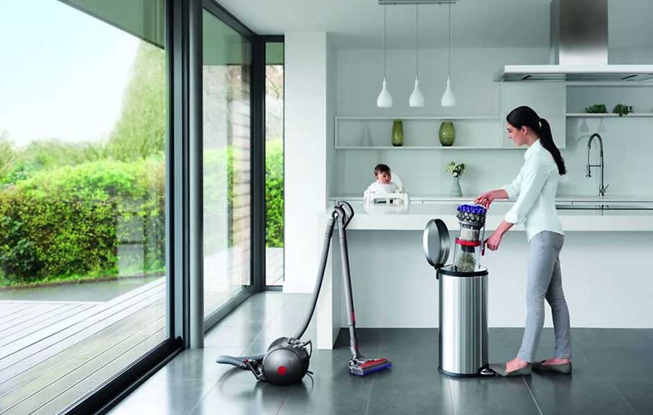 Une cuisine moderne avec un aspirateur Dyson, une poubelle en métal et de grandes fenêtres donnant sur un jardin.