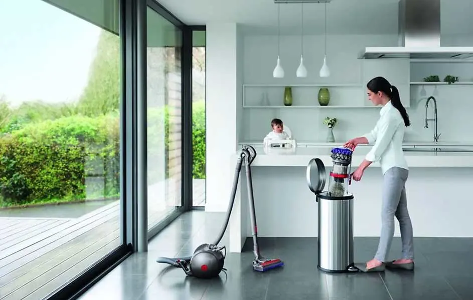 Une cuisine moderne avec un aspirateur Dyson, une poubelle en métal et de grandes fenêtres donnant sur un jardin.
