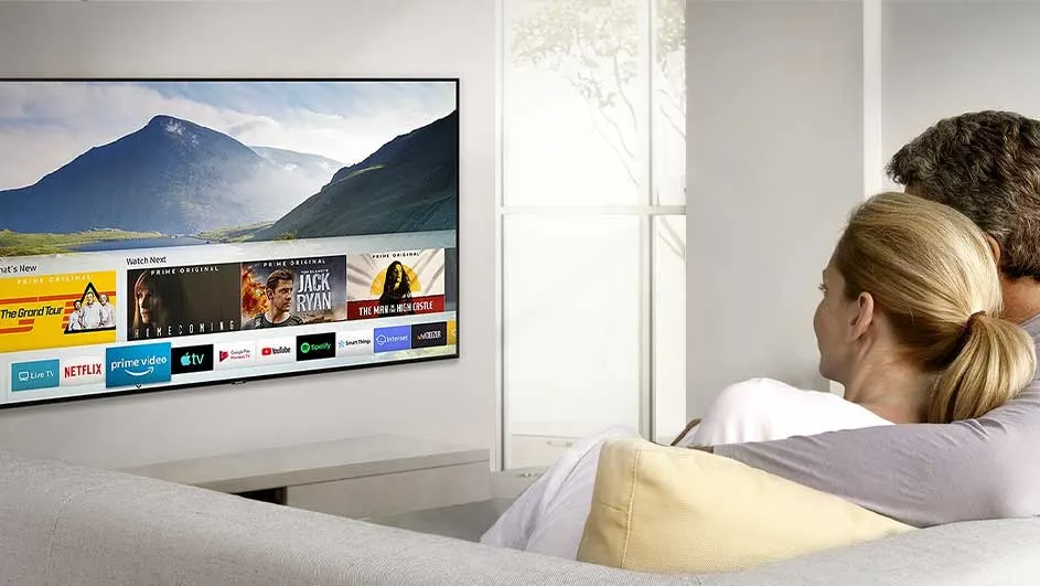Een grijze sofa voor een witte muur met een tv die een berglandschap en streamingdiensten weergeeft.