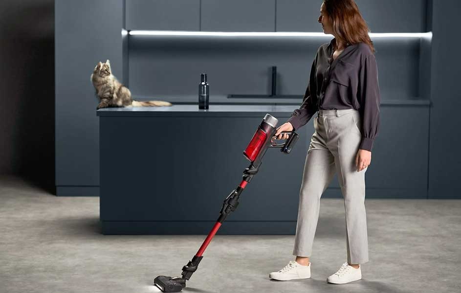 Une pièce moderne avec un aspirateur rouge et noir sur un sol gris. Un chat est assis sur un comptoir bleu.