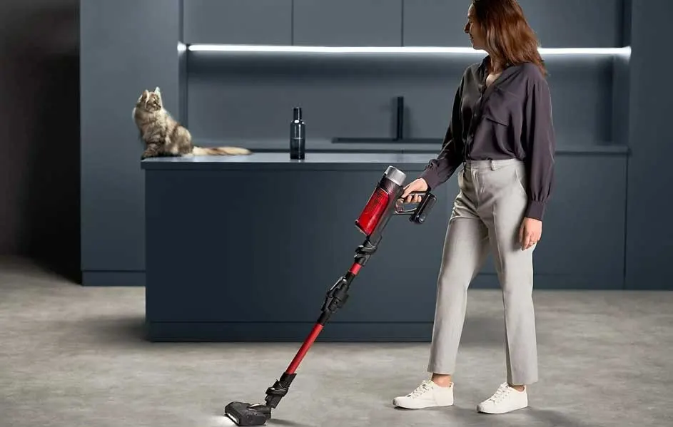 Une pièce moderne avec un aspirateur rouge et noir sur un sol gris. Un chat est assis sur un comptoir bleu.