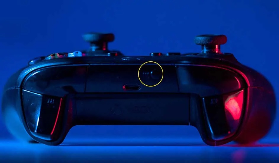 Une manette Xbox noire en gros plan, éclairée en bleu et rouge, est posée sur une surface avec le logo Xbox visible.