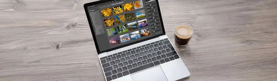A laptop displays photos next to a clear glass of coffee on a gray wood surface.