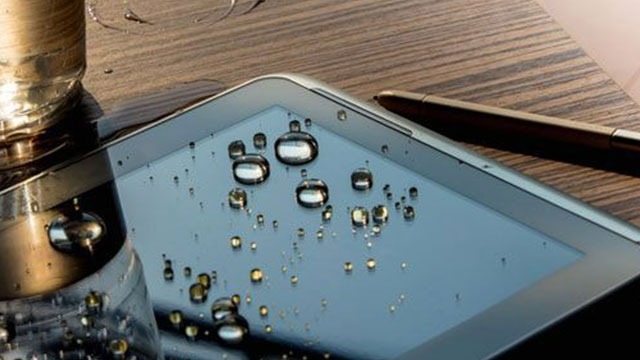 Un verre, une tablette avec des gouttes, et un stylet sur une table en bois.