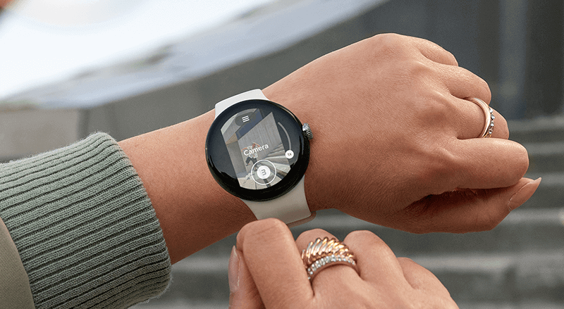 Een polshorloge met een witte band toont de camera-interface, gedragen met ringen.