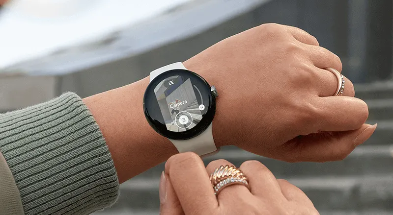Une montre intelligente ronde à écran noir avec un bracelet blanc est portée au poignet. L'écran affiche une application de caméra.