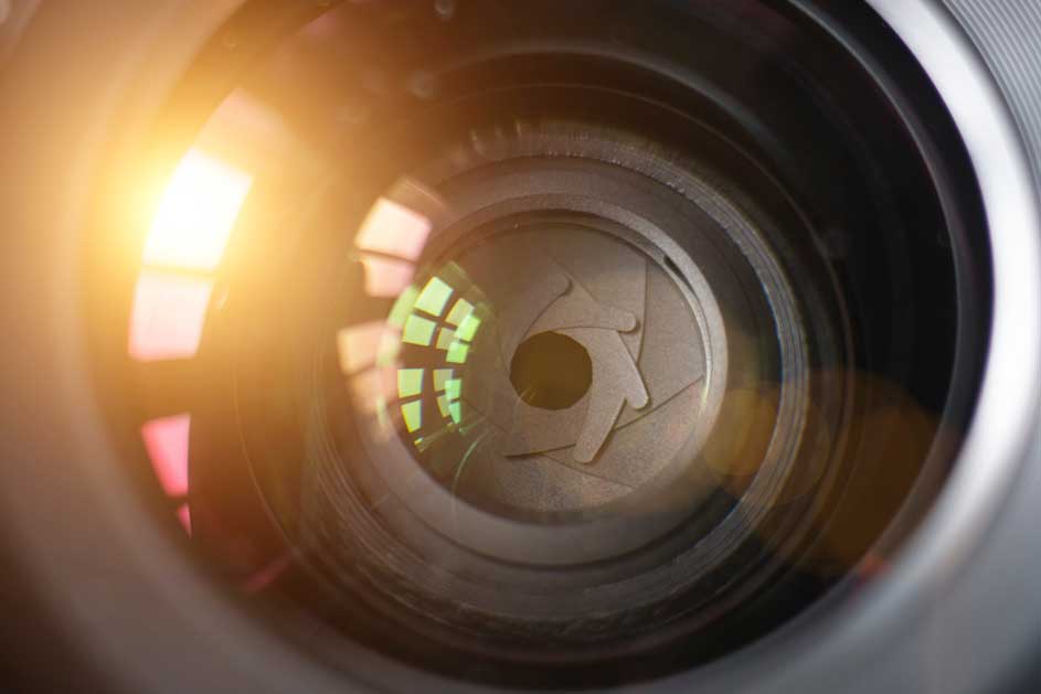 Een close-up van een cameralens met een diafragmaopening en reflecties van licht. De lens is grijs en zwart.