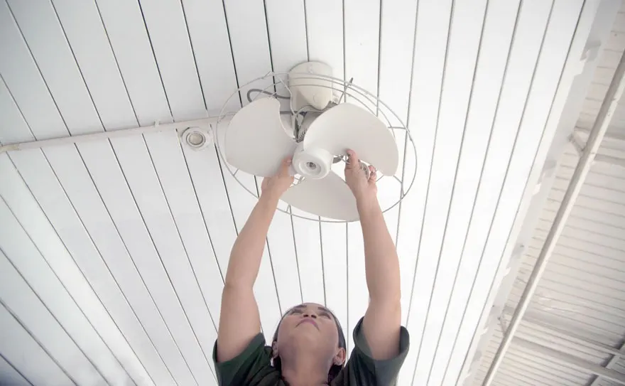 Un ventilateur de plafond blanc avec trois pales est fixé à un plafond à lattes blanches.
