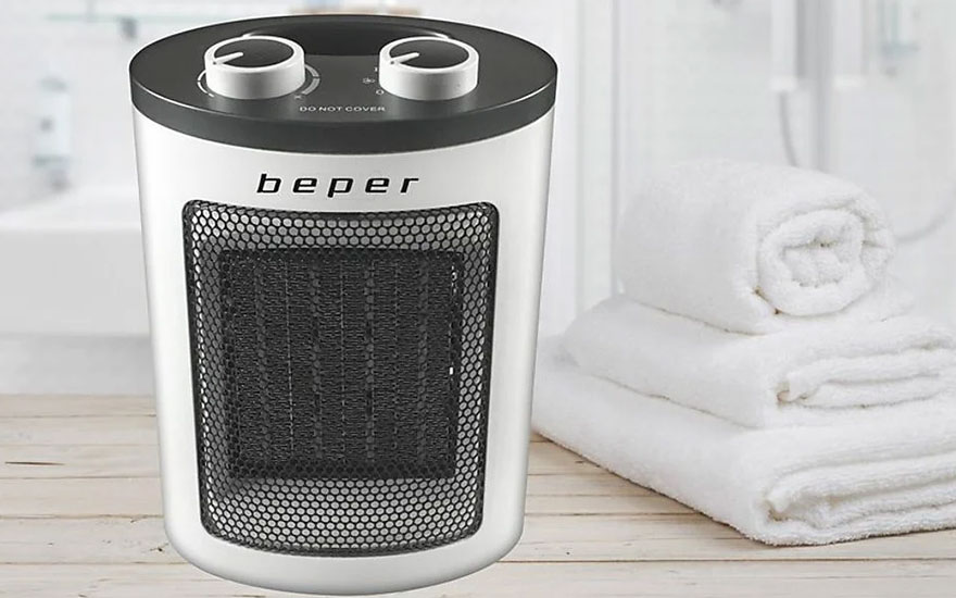 Een witte Beper kachel met een zwart rooster staat naast een stapel witte handdoeken op een houten oppervlak.