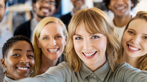 Un groupe de personnes souriantes posent ensemble, certains au premier plan et d'autres en arrière-plan, dans un cadre informel.