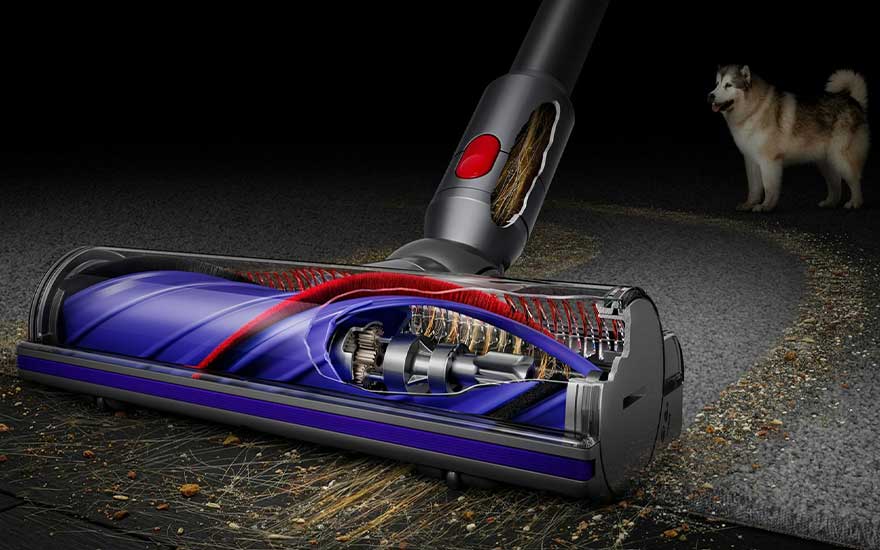 Aspirateur avec brosse bleue et rouge sur sol sale, avec un chien à l'arrière-plan.