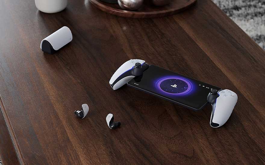 On a wooden table, wireless earbuds and a smartphone in a PlayStation controller grip are laid out neatly.