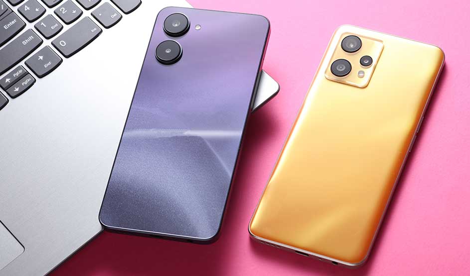 Deux smartphones, l’un violet et l’autre doré, sont posés près d’un ordinateur portable sur une surface rose vif.