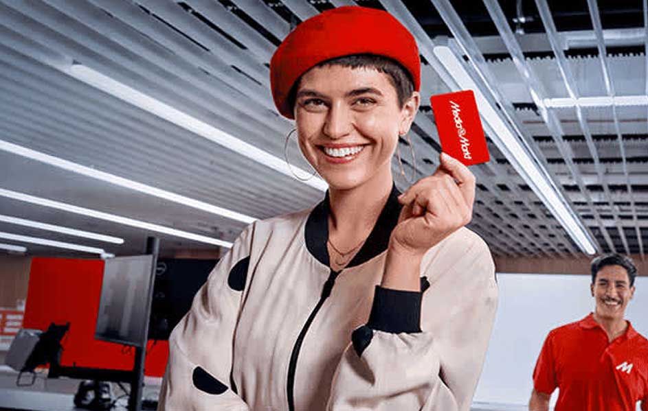 Een rode kaart van MediaMarkt wordt vastgehouden in een winkel met een wit plafond. Op de achtergrond staat rode apparatuur.