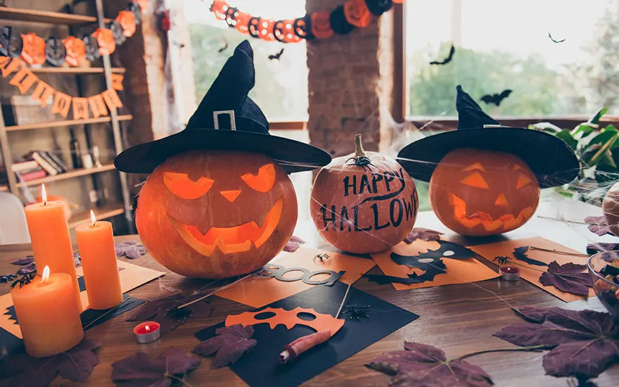 Décor d'Halloween avec des citrouilles sculptées, des bougies orange et des décorations de fête sur une table en bois.