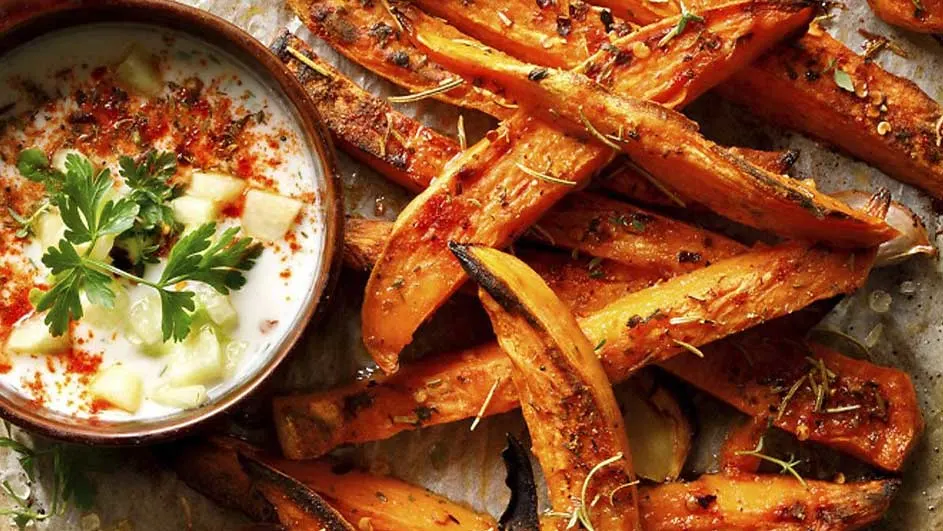 Gros plan d'un bol de sauce blanche avec des herbes à côté de quartiers de patates douces rôtis et assaisonnés.