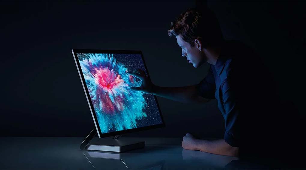 Un homme utilise un ordinateur avec un écran tactile affichant un motif abstrait bleu et rose sur un fond noir.