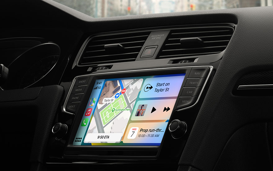 Zicht op een zwart dashboard van een auto met een aanraakscherm dat een navigatie-app en muziekbedieningselementen weergeeft.