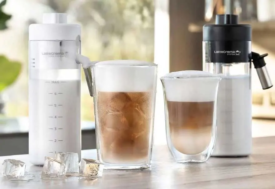 Twee glazen koffie met melk en ijs staan naast twee melkopschuimers op een houten tafel.